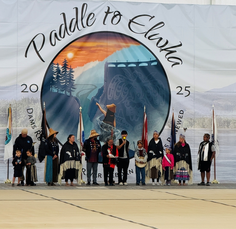Lower Elwha Klallam Tribe members stand in front of a large, white sign that reads 